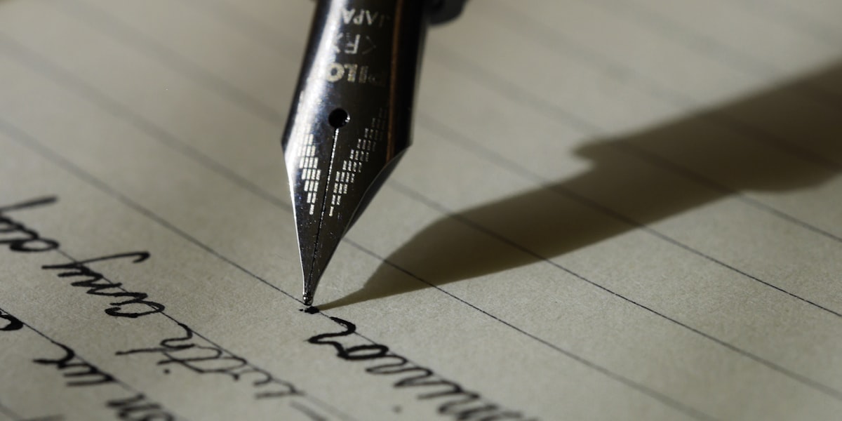 Person writing with a pen on paper at a desk